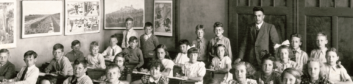Oude foto schoolklas met jongens en meisjes in de schoolbanken en de meester achterin de klas