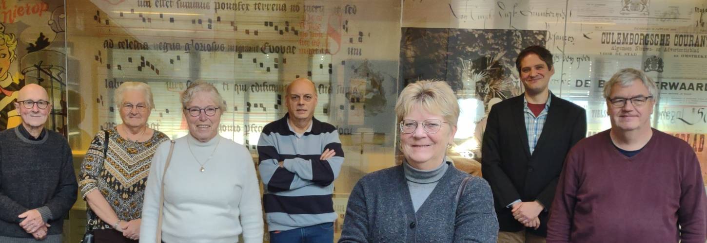 7 vrijwilligers poseren voor de glazen wand van de studiezaal bij het RAR : 3 vrouwen en vier mannen