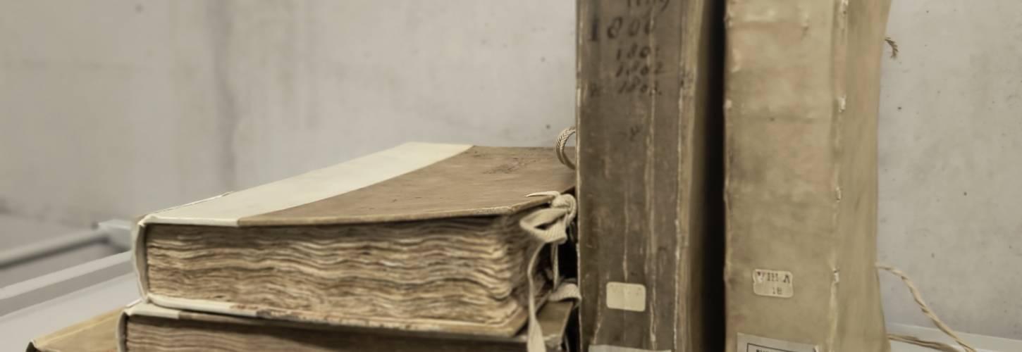 3 liggende oude boeken op elkaar met 2 staande ernaast