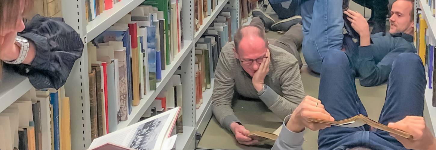 medewerkers RAR liggen in het bibliotheekdepot verdiept in boeken