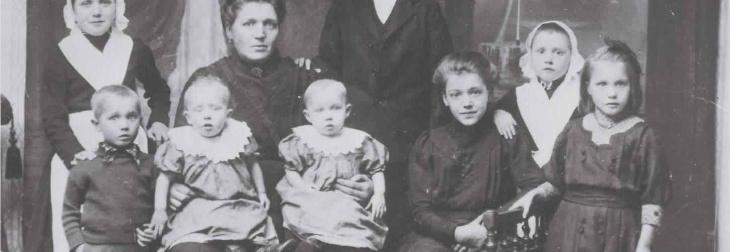 Groepsfoto uit 1912-1913 met een oudere dame met twee weeskinderen op schoot en om haar heen nog 6 grotere weeskinderen