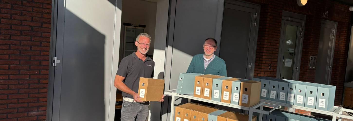 Twee mannen staan bij twee karren met archiefdozen