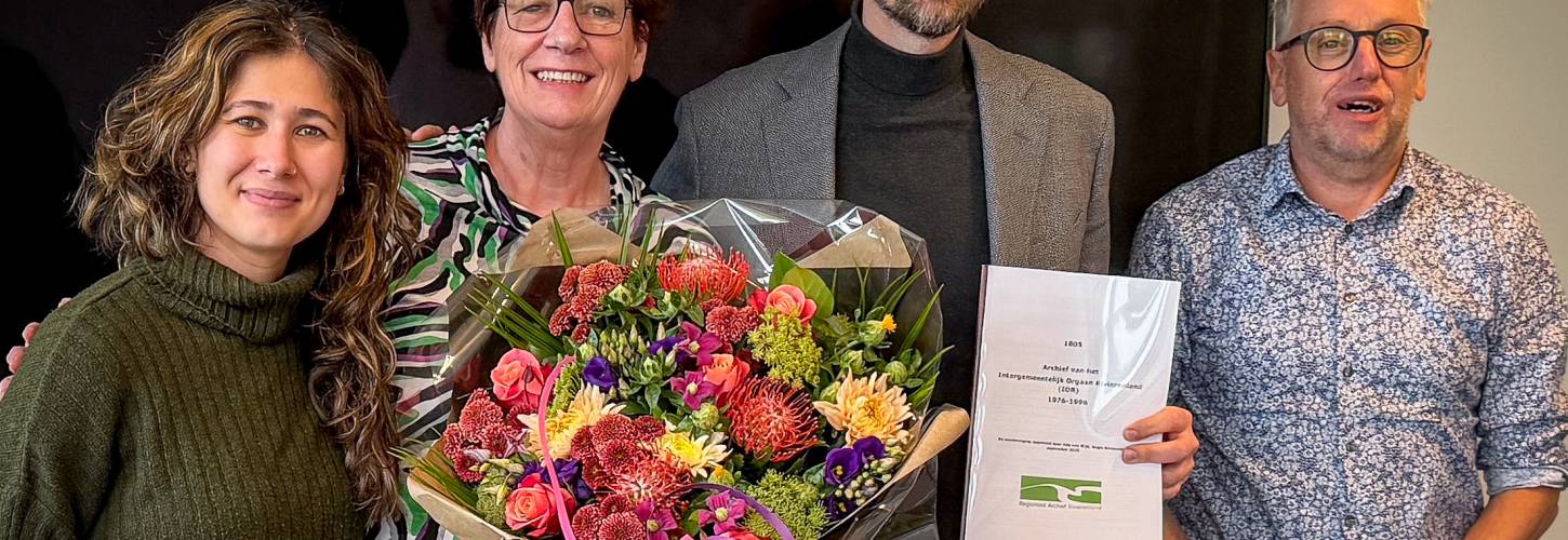 2 mannen en 2 vrouwen waarvan 1 vrouw een bos bloemen vasthoudt en 1 man een rapport omhoog houdt