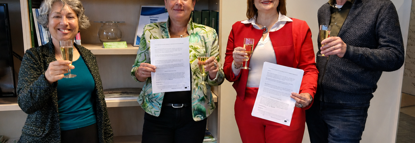 Vier personen, 3 vrouwen en 1 man, poseren in een kantoor voor een boekenkast met een glas in hun hand, 2 vrouwen houden een document omhoog
