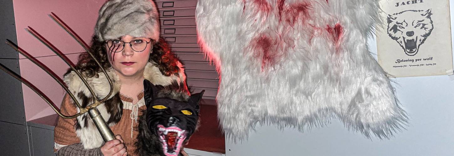 Medewerker Jonna verkleed als wolvenjager met hooivork, wolvenkop en bebloede schapenvacht