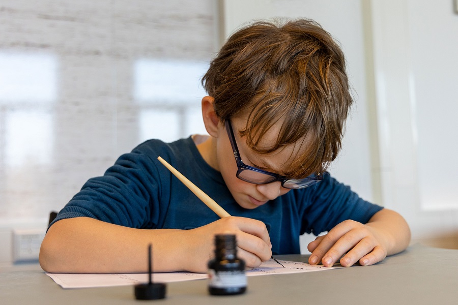 leerling schrijft met kroontjespen tijdens bezoekles dat wil ik zeggen bij het regionaal archief rivierenland. Jikke Fotografie en Vormgeving