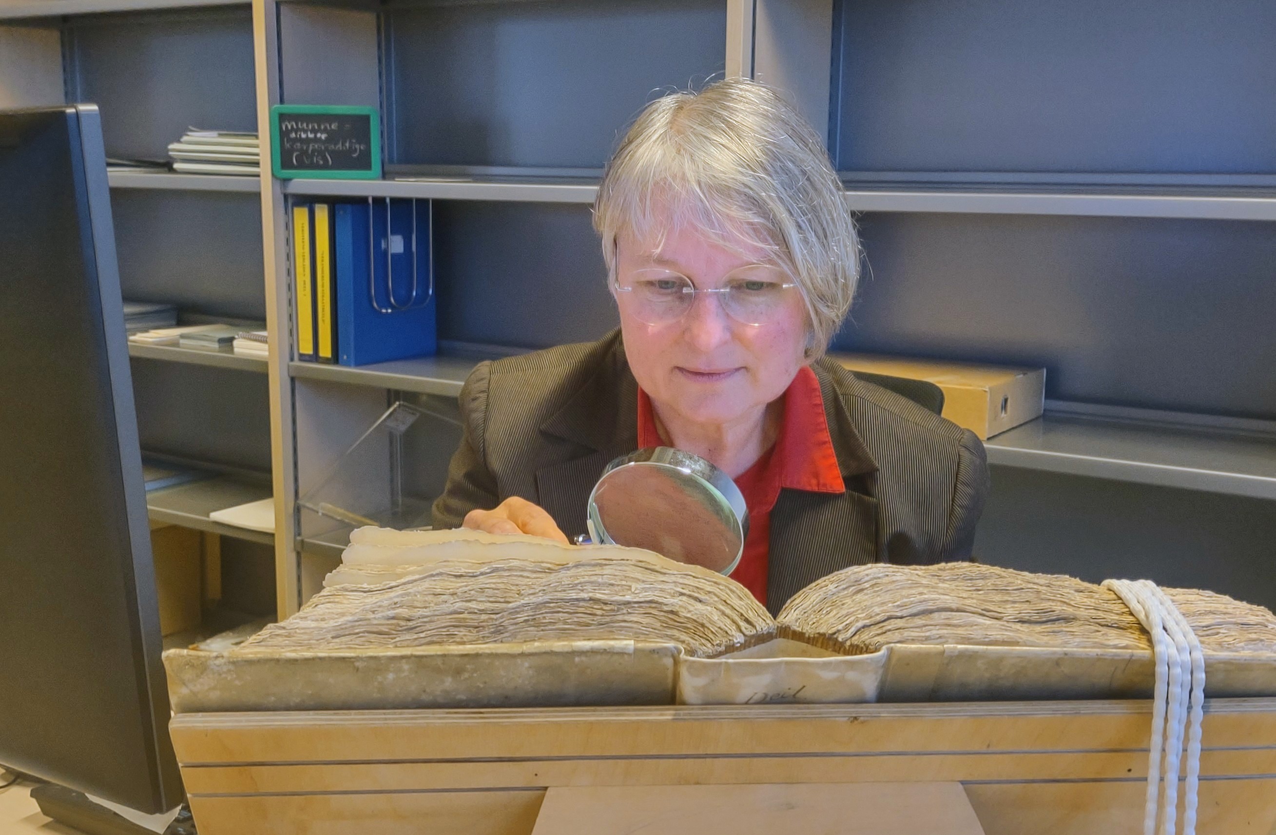 Ineke buigt zich met een loep over een groot oud dik boek