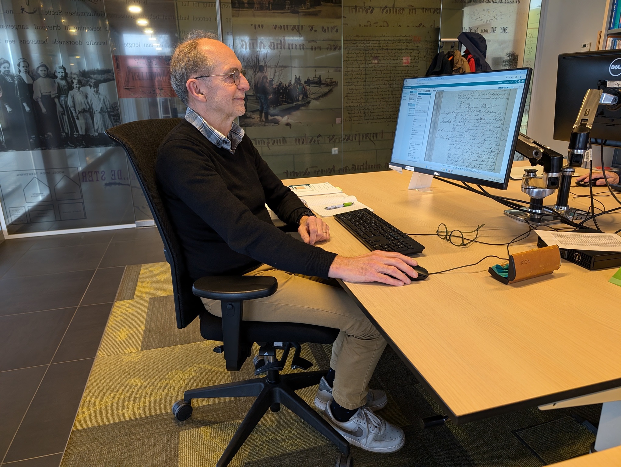 Guy zit achter een bureau met een computerscherm met een pagina uit een oud boek  te werken