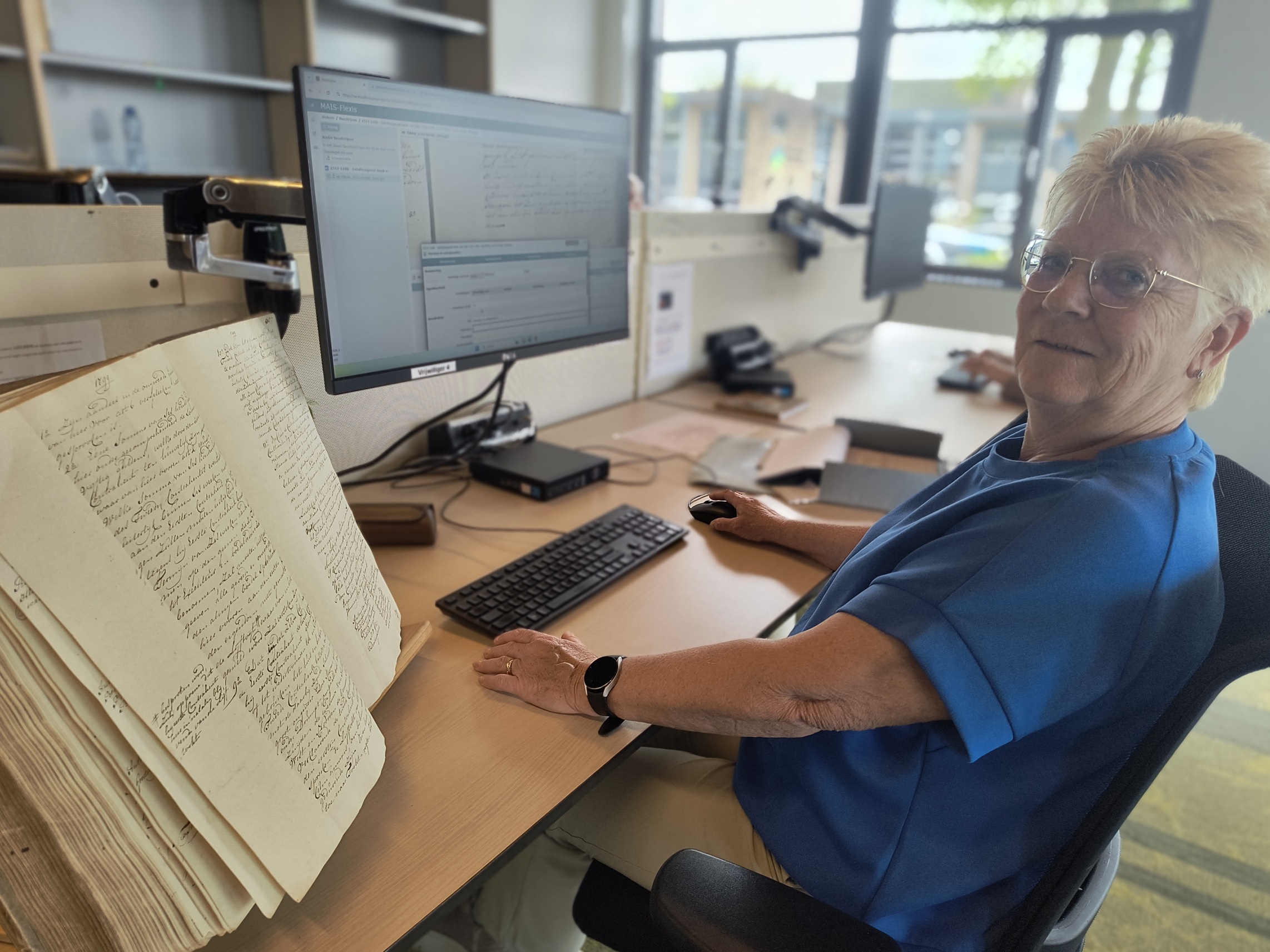 vrouw zit achter een pc scherm met naast zich een oud boek