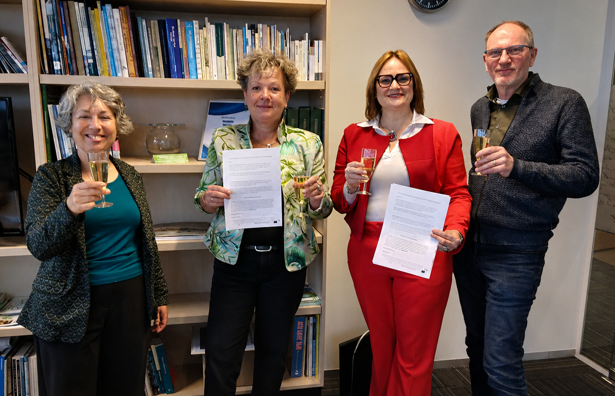 Vier personen, 3 vrouwen en 1 man, poseren in een kantoor voor een boekenkast met een glas in hun hand, 2 vrouwen houden een document omhoog