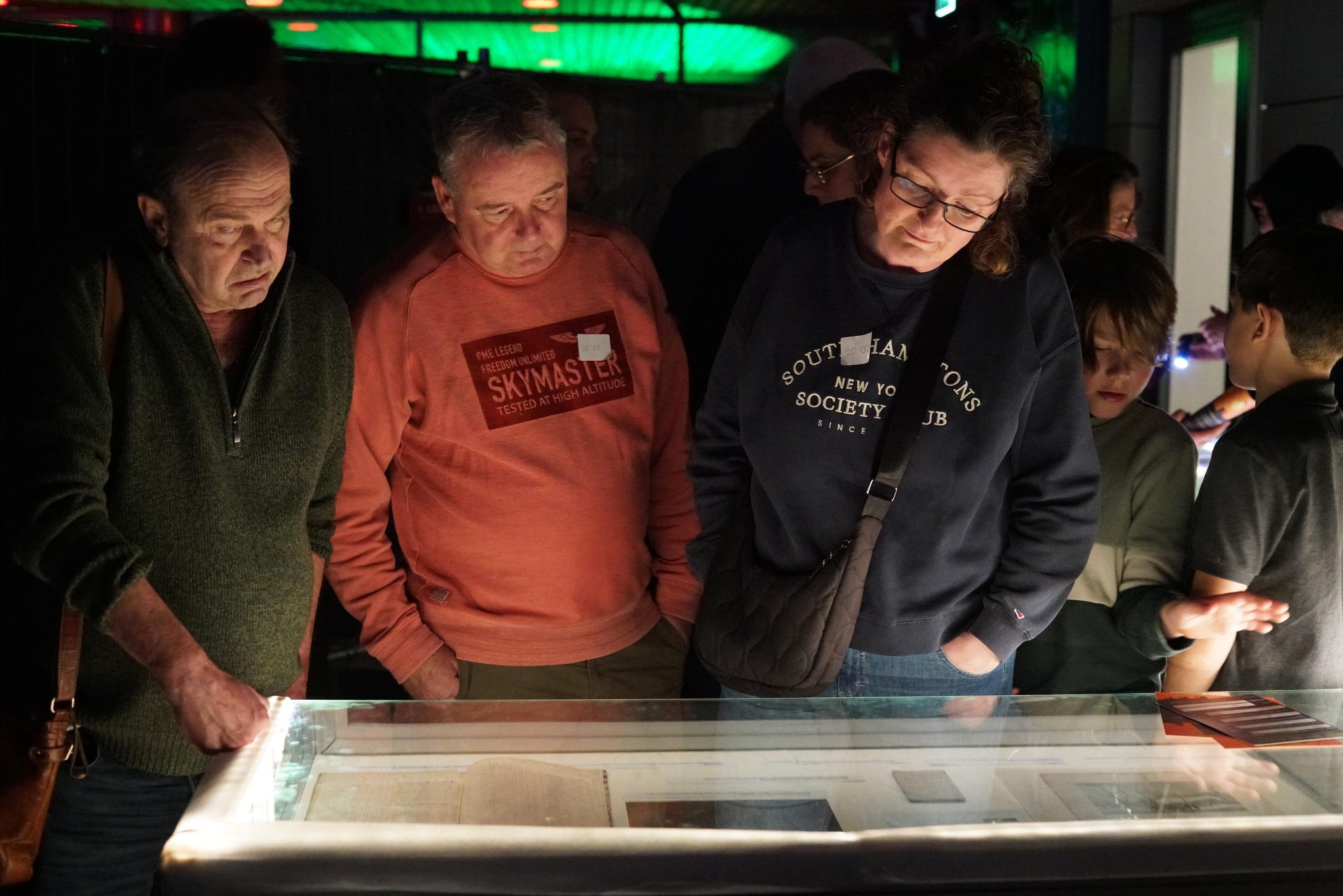 mensen bekijken archiefstukken in een verlichte vitrinekast