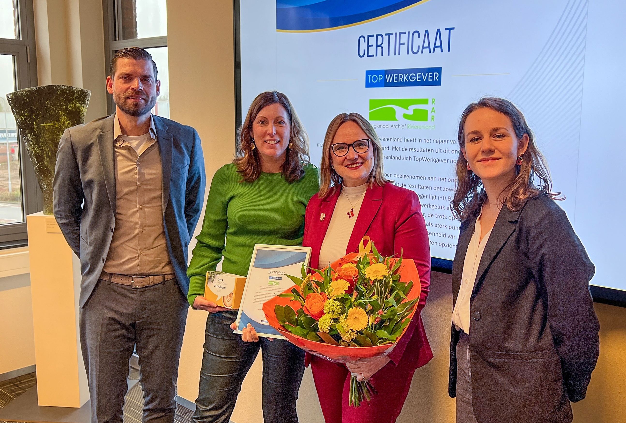 Twee medewerkers van Monitorgroep met in het midden Ella en Letty (samen het MT van het RAR) met bloemen en het certificaat